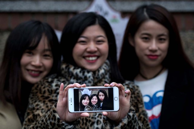 This picture taken on January 8, 2017 shows Hu Dongyuan (L), Wang Peng (C) and Peng Lin displaying their selfie in Shanghai. Strolling a tree-lined Shanghai street with friends, Hu Dongyuan pulls out her smartphone and does what millions of Chinese women do daily: take a selfie, digitally "beautify" their faces, and pop it on social media. Such virtual makeovers, typically involving lightening skin, smoothing out complexions and rounding the eyes, have propelled selfie-editing app Meitu to the top ranks of China downloads. / AFP PHOTO / Johannes EISELE / TO GO WITH China-technology-lifestyle-apps-selfies-Meitu, FEATURE by Albee ZHANG