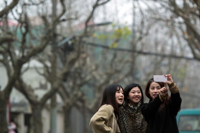 This picture taken on January 8, 2017 shows Hu Dongyuan (L), Wang Peng (C) and Peng Lin posing for a selfie in Shanghai. Strolling a tree-lined Shanghai street with friends, Hu Dongyuan pulls out her smartphone and does what millions of Chinese women do daily: take a selfie, digitally "beautify" their faces, and pop it on social media. Such virtual makeovers, typically involving lightening skin, smoothing out complexions and rounding the eyes, have propelled selfie-editing app Meitu to the top ranks of China downloads. / AFP PHOTO / Johannes EISELE / TO GO WITH China-technology-lifestyle-apps-selfies-Meitu, FEATURE by Albee ZHANG