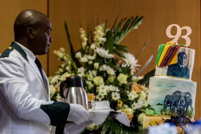 A waiter walks past a cake bearing a portrait of Zimbabwe's President Robert Mugabe during a private ceremony to celebrate Mugabe's 93rd birthday on February 21, 2017 in Harare.  Mugabe, the world's oldest national ruler, turned 93, using a long and occasionally rambling interview to vow to remain in power despite growing signs of frailty. / AFP PHOTO / Jekesai NJIKIZANA