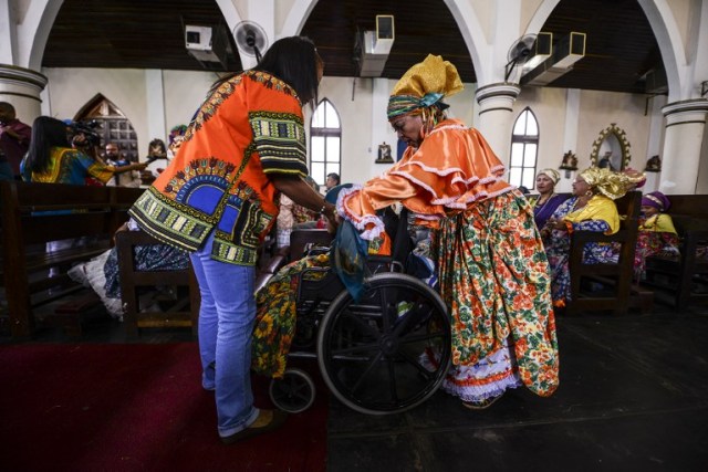 Women dressed as "madamas" attend a mass before the beginning of the Carnival in El Callao, in Bolivar state, Venezuela on February 26, 2017. El Callao's carnival was recently named Unesco's Intangible Cultural Heritage of Humanity and is led by the madamas, the pillars of Callaoense identity representing Antillean matrons considered the communicators of values, who dance and wear colourful dresses. / AFP PHOTO / JUAN BARRETO