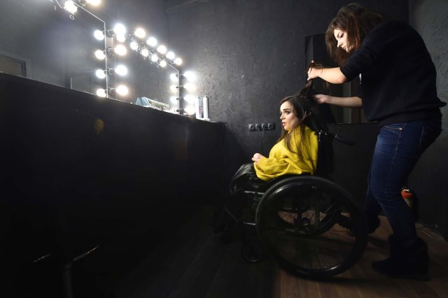 TO GO WITH AFP STORY BY OLGA SHYLENKO A makeup artist works on the hair of Ukrainian model Alexandra Kutas, who is in a wheelchair from a very early age due to a spinal cord injury resulting from a doctor's mistake at birth, prior to a photo and video fashion shoot in Kiev on January 25, 2017. Kutas, 23, is Ukraine's first model with a disability to headline a runway event of this level, after covering a long and thorny path for her dream to come true. / AFP PHOTO / Sergei SUPINSKY / ?The erroneous mention[s] appearing in the metadata of this photo by Sergei SUPINSKY has been modified in AFP systems in the following manner: [a spinal cord injury resulting from a doctor's mistake at birth] instead of [cerebral palsy]. Please immediately remove the erroneous mention[s] from all your online services and delete it (them) from your servers. If you have been authorized by AFP to distribute it (them) to third parties, please ensure that the same actions are carried out by them. Failure to promptly comply with these instructions will entail liability on your part for any continued or post notification usage. Therefore we thank you very much for all your attention and prompt action. We are sorry for the inconvenience this notification may cause and remain at your disposal for any further information you may require.?