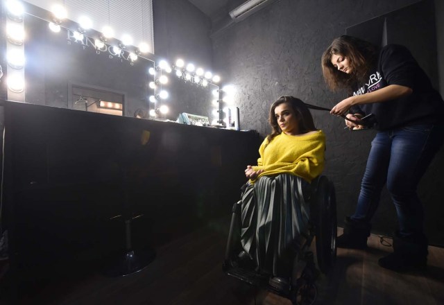 TO GO WITH AFP STORY BY OLGA SHYLENKO A makeup artist works on the hair of Ukrainian model Alexandra Kutas, who is in a wheelchair from a very early age due to a spinal cord injury resulting from a doctor's mistake at birth, prior to a photo and video fashion shoot in Kiev on January 25, 2017. Kutas, 23, is Ukraine's first model with a disability to headline a runway event of this level, after covering a long and thorny path for her dream to come true. / AFP PHOTO / Sergei SUPINSKY / ?The erroneous mention[s] appearing in the metadata of this photo by Sergei SUPINSKY has been modified in AFP systems in the following manner: [a spinal cord injury resulting from a doctor's mistake at birth] instead of [cerebral palsy]. Please immediately remove the erroneous mention[s] from all your online services and delete it (them) from your servers. If you have been authorized by AFP to distribute it (them) to third parties, please ensure that the same actions are carried out by them. Failure to promptly comply with these instructions will entail liability on your part for any continued or post notification usage. Therefore we thank you very much for all your attention and prompt action. We are sorry for the inconvenience this notification may cause and remain at your disposal for any further information you may require.?