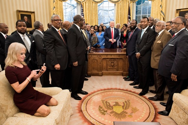 Counselor to the President Kellyanne Conway (L) checks her phone after taking a photo as US President Donald Trump and leaders of historically black universities and colleges pose for a group photo in the Oval Office of the White House before a meeting with US Vice President Mike Pence February 27, 2017 in Washington, DC. / AFP PHOTO / Brendan Smialowski