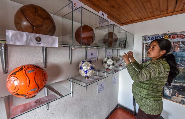 An employee of the Museum of the Soccer Ball cleans glass cases in Mongui, in the Colombian department of Boyaca, on February 13, 2017. Mongui, in the central mountains of Colombia, has about 20 football factories that make balls mainly for football and micro-football. About a quarter of the town's 4,900 inhabitants work in these factories. / AFP PHOTO / Luis ACOSTA