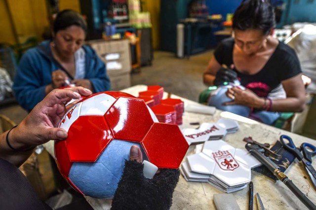 Workers make footballs at a ball factory in Mongui, in the Colombian department of Boyaca, on February 13, 2017. Mongui, in the central mountains of Colombia, has about 20 football factories that make balls mainly for football and micro-football. About a quarter of the town's 4,900 inhabitants work in these factories. / AFP PHOTO / Luis ACOSTA