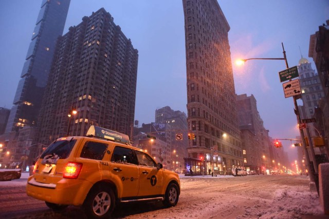 A yellow cab is on the lookout for customers near Madison Square Park at the foot of the Flatiron building in Manhattan during a snowstorm in New York on March 14, 2017. Winter Storm Stella dumped snow and sleet Tuesday across the northeastern United States where thousands of flights were canceled and schools closed, but appeared less severe than initially forecast. After daybreak the National Weather Service (NWS) revised down its predicted snow accumulation for the city of New York, saying that the storm had moved across the coast. / AFP PHOTO / ERIC BARADAT