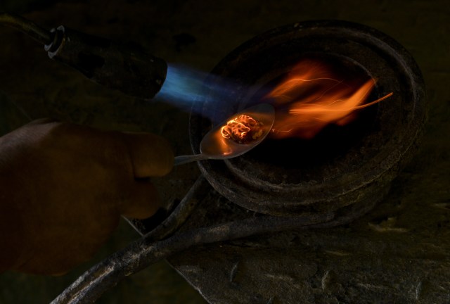 A worker melts a gold-mercury amalgam to extract the gold, at a gold mine in El Callao, Bolivar state, southeastern Venezuela on February 25, 2017. Although life in the mines of eastern Venezuela is hard and dangerous, tens of thousands from all over the country head for the mines daily in overcrowded trucks, pushed by the rise in gold prices and by the severe economic crisis affecting the country, aggravated recently by the drop in oil prices. / AFP PHOTO / JUAN BARRETO