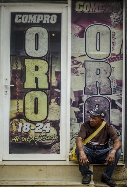 A man sits outside a store reading "We buy gold" in El Callao, Bolivar state, southeastern Venezuela on February 25, 2017. Although life in the mines of eastern Venezuela is hard and dangerous, tens of thousands from all over the country head for the mines daily in overcrowded trucks, pushed by the rise in gold prices and by the severe economic crisis affecting the country, aggravated recently by the drop in oil prices. / AFP PHOTO / JUAN BARRETO