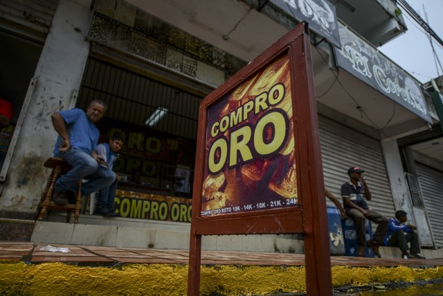 Men sit outside a store reading "We buy gold" in El Callao, Bolivar state, southeastern Venezuela on February 25, 2017. Although life in the mines of eastern Venezuela is hard and dangerous, tens of thousands from all over the country head for the mines daily in overcrowded trucks, pushed by the rise in gold prices and by the severe economic crisis affecting the country, aggravated recently by the drop in oil prices. / AFP PHOTO / JUAN BARRETO