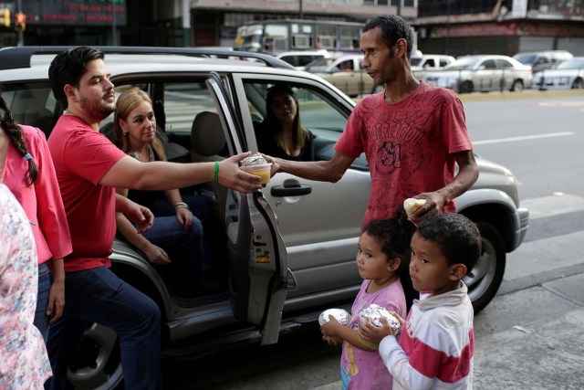 Diego Prada (L), a volunteer of the Make The Difference (Haz La Diferencia) charity initiative, gives a cup of soup and an arepa to a man in a street of Caracas, Venezuela March12, 2017. Picture taken March 12, 2017. REUTERS/Marco Bello