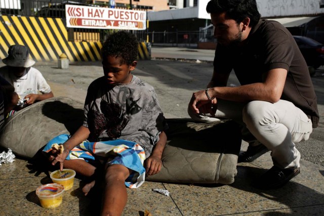 A volunteer of Make The Difference (Haz La Diferencia) charity initiative speaks with a homeless child after giving him a cup of soup and an arepa in a street of Caracas, Venezuela March 5, 2017. Picture taken March 5, 2017. REUTERS/Marco Bello