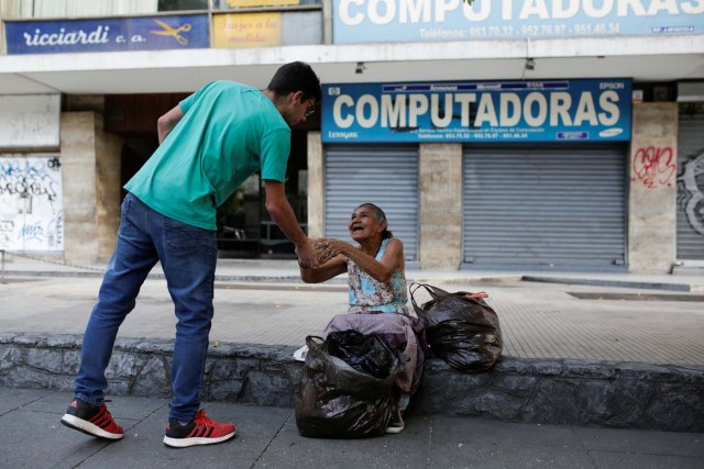 Mariano Marquez (L), a volunteer of Make The Difference (Haz La Diferencia) charity initiative, gives a cup of soup and an arepa to a homeless woman in a street of Caracas, Venezuela March12, 2017. Picture taken March 12, 2017. REUTERS/Marco Bello