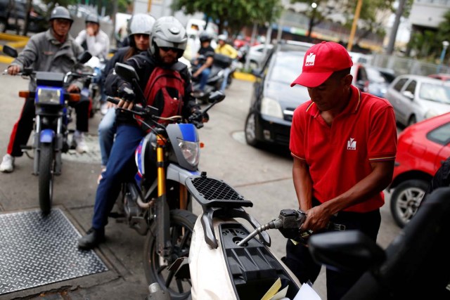 A gas station worker pumps gas into a motorcycle as people wait in line to fill the tanks of their vehicles at a gas station of the state oil company PDVSA in Caracas, Venezuela March 22, 2017. REUTERS/Carlos Garcia Rawlins