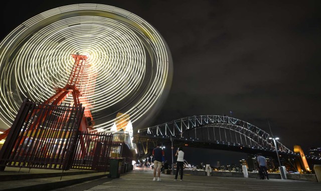 The ferris wheel at Luna Park and Sydney Harbour Bridge are seen before being plunged into darkness for the Earth Hour environmental campaign in Sydney on March 25, 2017. The lights went out on two of Sydney's most famous landmarks for the 10th anniversary of the climate change awareness campaign Earth Hour, among the first landmarks around the world to dim their lights for the event. / AFP PHOTO / PETER PARKS