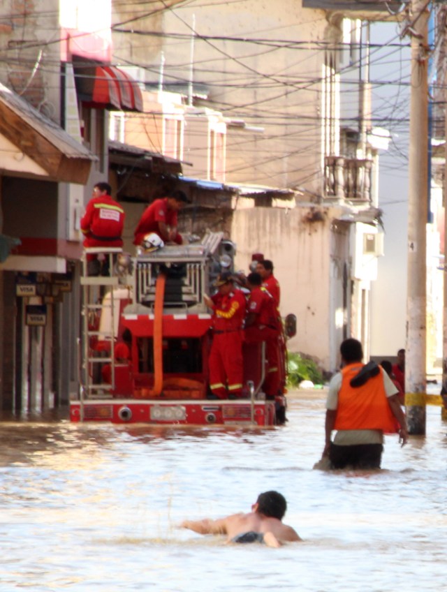 Residents in the city of Piura, 1,000 kilometres north of Lima, wade through water on the streets on March 27, 2017, after nearly 15 hours of rain caused the Piura River to overflow, flooding neighbourhoods in most of the city.  The El Nino climate phenomenon is causing muddy flash floods and rivers to overflow along the entire Peruvian coast, isolating communities and neighborhoods. Most cities face water shortages as water lines have been compromised by mud and debris. / AFP PHOTO / PATRICIA LACHIRA / BEST QUALITY AVAILABLE