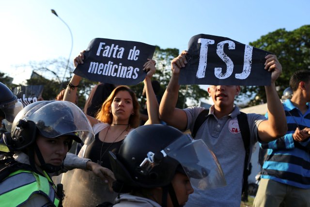 Opposition supporters holding placard that reads, (L-R) "Shortage of medicines" and "TSJ", shout slogans in front of the riot police during a protest in Caracas, Venezuela March 30, 2017. REUTERS/Carlos Garcia Rawlins