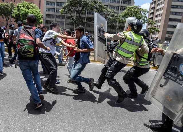 Venezuela's opposition activists clash with riot police agents during a protest against Nicolas Maduro's government in Caracas on April 4, 2017. Protesters clashed with police in Venezuela Tuesday as the opposition mobilized against moves to tighten President Nicolas Maduro's grip on power. Protesters hurled stones at riot police who fired tear gas as they blocked the demonstrators from advancing through central Caracas, where pro-government activists were also planning to march.  / AFP PHOTO / JUAN BARRETO