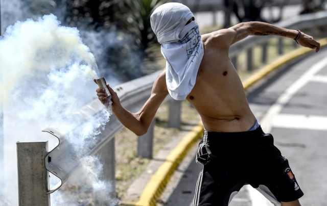An opposition activists throws back at riot police a tear gas grenade during a protest against President Nicolas Maduro's government in Caracas on April 4, 2017.  Activists clashed with police in Venezuela Tuesday as the opposition mobilized against moves to tighten President Nicolas Maduro's grip on power. Protesters hurled stones at riot police who fired tear gas as they blocked the demonstrators from advancing through central Caracas, where pro-government activists were also planning to march. / AFP PHOTO / JUAN BARRETO