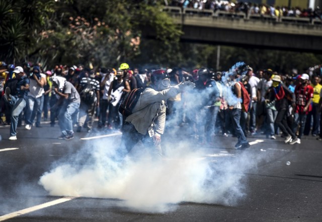 A demonstrator throws back a tear gas grenade thrown by riot police during a protest against President Nicolas Maduro's government in Caracas on April 4, 2017.  Activists clashed with police in Venezuela Tuesday as the opposition mobilized against moves to tighten President Nicolas Maduro's grip on power. Protesters hurled stones at riot police who fired tear gas as they blocked the demonstrators from advancing through central Caracas, where pro-government activists were also planning to march. / AFP PHOTO / JUAN BARRETO