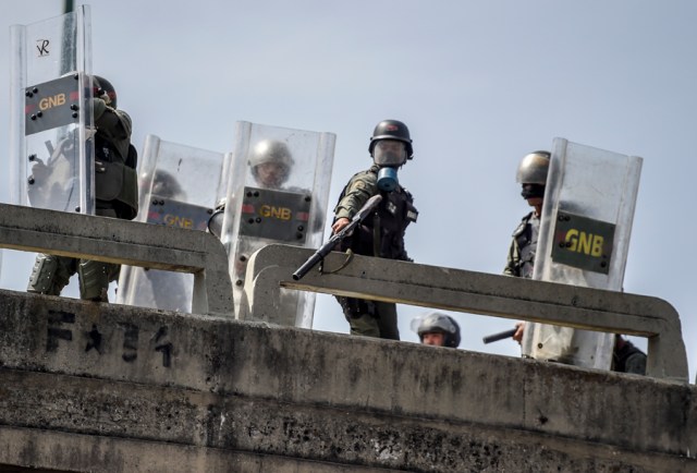 A Venezuelan National Guard trooper in riot gear aims his grenade launcher at demonstrators from a footbridge during a protest against President Nicolas Maduro's government in Caracas on April 4, 2017.  Activists clashed with police in Venezuela Tuesday as the opposition mobilized against moves to tighten President Nicolas Maduro's grip on power. Protesters hurled stones at riot police who fired tear gas as they blocked the demonstrators from advancing through central Caracas, where pro-government activists were also planning to march. / AFP PHOTO / JUAN BARRETO