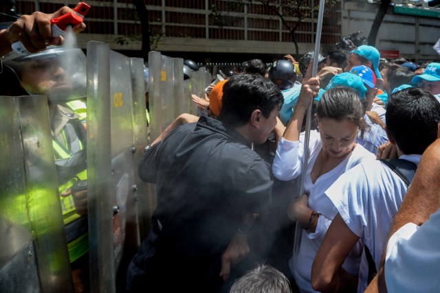 Venezuelan opposition leader Maria Corina Machado (R) is sprayed with tear gas by riot police (top-L) during a protest against President Nicolas Maduro's government in Caracas on April 4, 2017.  Activists clashed with police in Venezuela Tuesday as the opposition mobilized against moves to tighten President Nicolas Maduro's grip on power. Protesters hurled stones at riot police who fired tear gas as they blocked the demonstrators from advancing through central Caracas, where pro-government activists were also planning to march. / AFP PHOTO / FEDERICO PARRA
