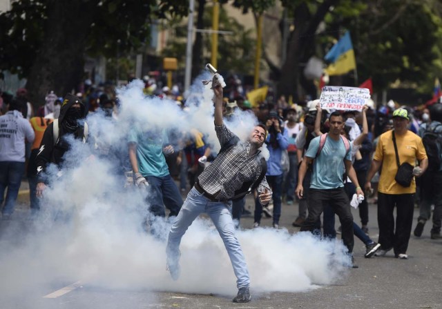 A demonstrator against Nicolas Maduro's government returns a tear gas during clashes with riot police at eastern Caracas on April 8, 2017. The opposition is accusing pro-Maduro Supreme Court judges of attempting an internal "coup d'etat" for attempting to take over the opposition-majority legislature's powers last week. The socialist president's supporters held counter-demonstrations on Thursday, condemning Maduro's opponents as "imperialists" plotting with the United States to oust him. / AFP PHOTO / JUAN BARRETO