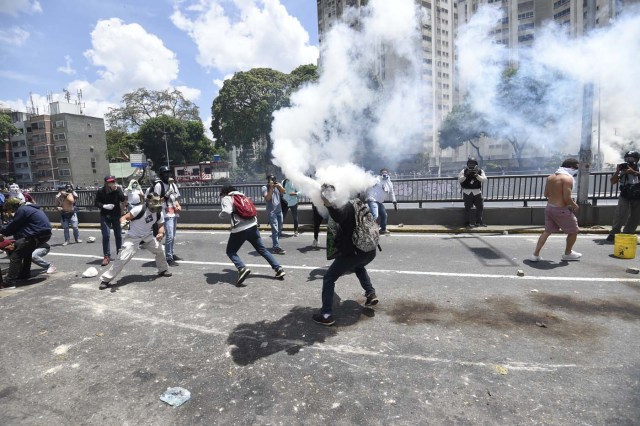 A demonstrator against Nicolas Maduro's government tries to return a tear gas during clashes with riot police at eastern Caracas on April 8, 2017. The opposition is accusing pro-Maduro Supreme Court judges of attempting an internal "coup d'etat" for attempting to take over the opposition-majority legislature's powers last week. The socialist president's supporters held counter-demonstrations on Thursday, condemning Maduro's opponents as "imperialists" plotting with the United States to oust him. / AFP PHOTO / JUAN BARRETO