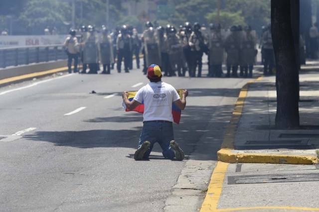 A demonstrator against Nicolas Maduro's government deploys a Venezuelan flag during clashes with riot police in Caracas on April 8, 2017. The opposition is accusing pro-Maduro Supreme Court judges of attempting an internal "coup d'etat" for attempting to take over the opposition-majority legislature's powers last week. The socialist president's supporters held counter-demonstrations on Thursday, condemning Maduro's opponents as "imperialists" plotting with the United States to oust him. / AFP PHOTO / JUAN BARRETO