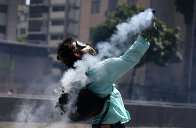 A demonstrator throws back a tear gas canister during clashes with riot police during a rally in Caracas, Venezuela, April 8, 2017. REUTERS/Carlos Garcia Rawlins