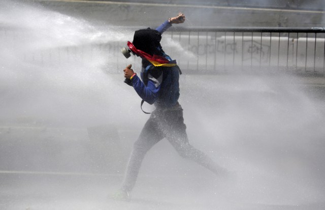 A demonstrator gets hit with a water canon while clashing with riot police during a rally in Caracas, Venezuela, April 8, 2017. REUTERS/Marco Bello