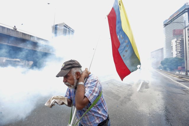 CAR216. CARACAS (VENEZUELA), 19/04/2017 - Un hombre se protege de los gases lacrimógenos durante una protesta contra el Gobierno venezolano hoy, miércoles 19 de abril de 2017, en Caracas (Venezuela). Centenares de opositores en distintos puntos de caracas se enfrentaron hoy a los cuerpos de seguridad para mantenerse en las calles protestando, pese al uso de bombas lacrimógenas por parte de las fuerzas policiales para dispersar y bloquear el paso de las marchas. EFE/CRISTIAN HERNANDEZ