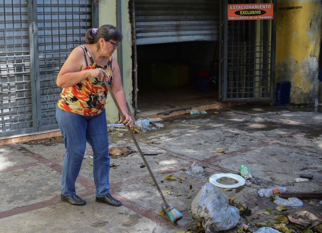 A woman sweeps the sidewalk in Caracas on April 20, 2017 a day after businesses were looted after demonstrations pro and against the government of Venezuelan President Nicolas Maduro. Venezuelan riot police fired tear gas Thursday at groups of protesters seeking to oust Maduro, who have vowed new mass marches after a day of deadly unrest. On the eve, hundreds of thousands of people fed up with food shortages and demanding elections joined protest marches in Caracas and several other cities while thousands of Maduro's supporters held a counter-rally in central Caracas.  / AFP PHOTO / Ronaldo SCHEMIDT