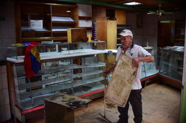 A man picks up the mess at a business in Caracas on April 20, 2017 a day after looting occurred after demonstrations pro and against the government of Venezuelan President Nicolas Maduro. Venezuelan riot police fired tear gas Thursday at groups of protesters seeking to oust Maduro, who have vowed new mass marches after a day of deadly unrest. On the eve, hundreds of thousands of people fed up with food shortages and demanding elections joined protest marches in Caracas and several other cities while thousands of Maduro's supporters held a counter-rally in central Caracas.  / AFP PHOTO / Ronaldo SCHEMIDT