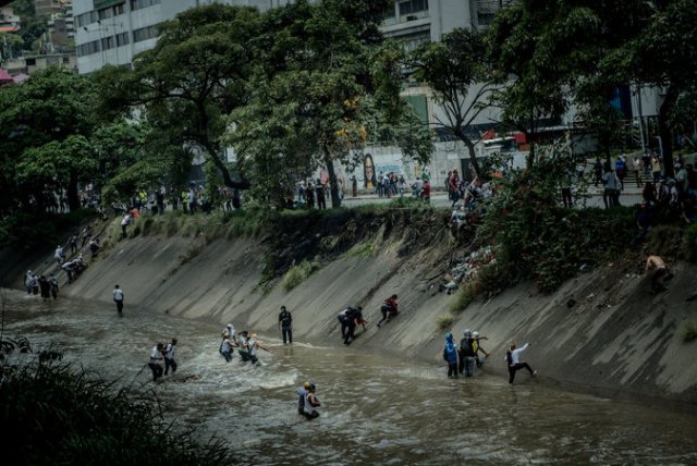 Manifestantes escapan de las bombas lacrimógenas el miércoles lanzándose al Guaire, un río contaminado en Caracas. Credit Meridith Kohut para The New York Times