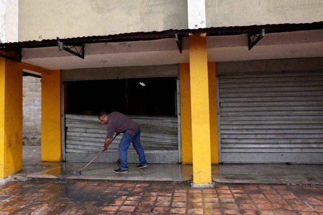 A man cleans the floor next to the broken door of a supermarket which was looted in Caracas, Venezuela April 21, 2017. REUTERS/Carlos Garcia Rawlins