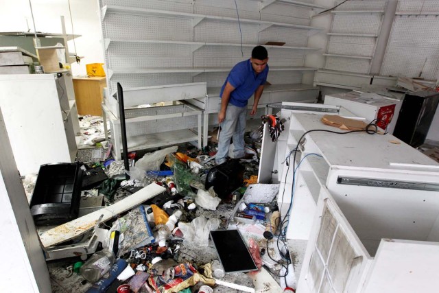A worker looks for valuables scattered in the damaged goods in a convenience store, after it was looted in Caracas, Venezuela April 21, 2017. REUTERS/Christian Veron