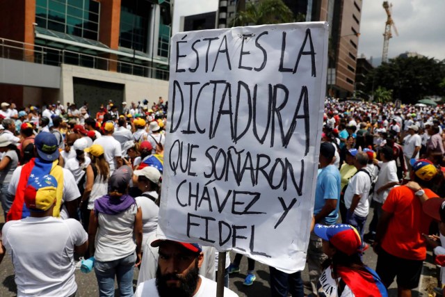 A demonstrator holds a placard as he takes part in a rally to honour victims of violence during a protest against Venezuela's President Nicolas Maduro's government in Caracas, Venezuela, April 22, 2017. The placard reads "This is the dictatorship who dreamed, Chavez and Fidel". REUTERS/Carlos Garcia Rawlins