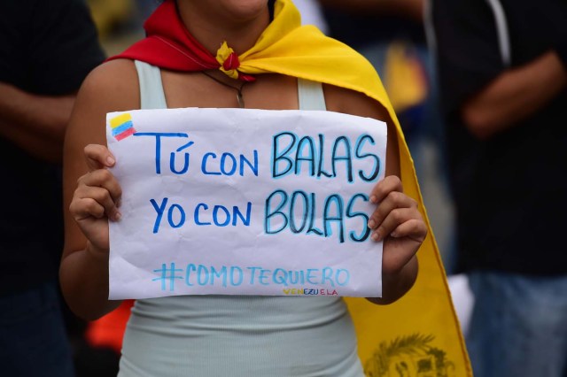 A Venezuelan opposition activist participating in a sit-in to block the Francisco Fajardo motorway carries a placard with a pun (in Spanish) that reads "You With Bullets, I With Balls", in Caracas, on April 24, 2017. Protesters plan Monday to block Venezuela's main roads including the capital's biggest motorway, triggering fears of further violence after three weeks of unrest left 21 people dead. / AFP PHOTO / RONALDO SCHEMIDT