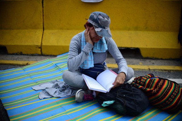 A Venezuelan opposition activist reads whilst participating in a sit-in to block the Francisco Fajardo motorway in Caracas, on April 24, 2017. Protesters plan Monday to block Venezuela's main roads including the capital's biggest motorway, triggering fears of further violence after three weeks of unrest left 21 people dead. / AFP PHOTO / RONALDO SCHEMIDT