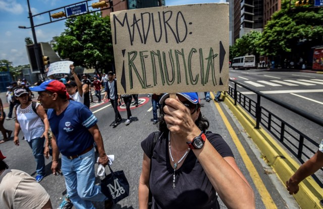 A Venezuelan opposition activist holds a placard reading "Maduro Quit" during a march against President Nicolas Maduro in Caracas, on April 24, 2017. Protesters rallied on Monday vowing to block Venezuela's main roads to raise pressure on Maduro after three weeks of deadly unrest that have left 21 people dead. Riot police fired rubber bullets and tear gas to break up one of the first rallies in eastern Caracas early Monday while other groups were gathering elsewhere, the opposition said.  / AFP PHOTO / Juan BARRETO