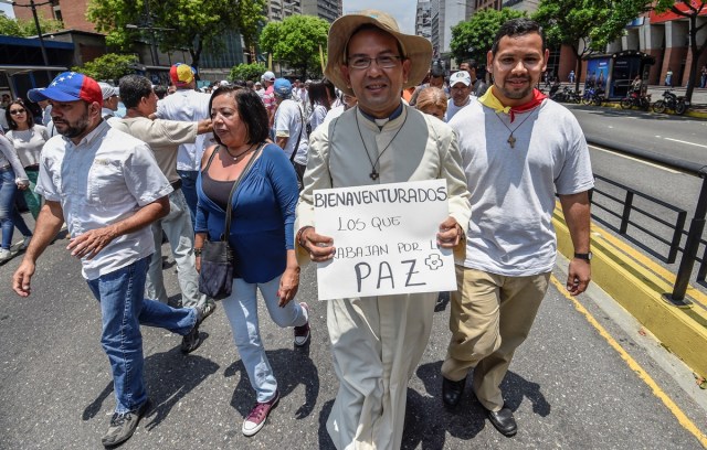 A priest joins opposition activists in a march against Venezuelan President Nicolas Maduro in Caracas, on April 24, 2017. Protesters rallied on Monday vowing to block Venezuela's main roads to raise pressure on Maduro after three weeks of deadly unrest that have left 21 people dead. Riot police fired rubber bullets and tear gas to break up one of the first rallies in eastern Caracas early Monday while other groups were gathering elsewhere, the opposition said.  / AFP PHOTO / Juan BARRETO