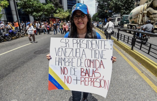 A Venezuelan opposition activist holds a placard reading "Mr. President, Venezuela is Hungry of Food Not of Bullets. No More Repression" as she marches against President Nicolas Maduro in Caracas, on April 24, 2017. Protesters rallied on Monday vowing to block Venezuela's main roads to raise pressure on Maduro after three weeks of deadly unrest that have left 21 people dead. Riot police fired rubber bullets and tear gas to break up one of the first rallies in eastern Caracas early Monday while other groups were gathering elsewhere, the opposition said.  / AFP PHOTO / Juan BARRETO