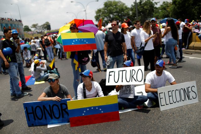 Opposition supporters holding Venezuelan flags and placards that read, "Honor", "Future" and "Elections", sit on the floor during a rally against Venezuela's President Nicolas Maduro in Caracas