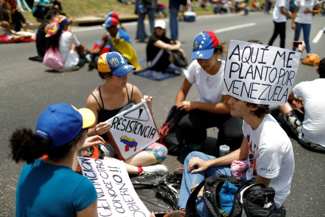 An opposition supporter wearing a placard on his head that reads, "Here I'll stay for Venezuela", sits on the floor with others during a rally against Venezuela's President Nicolas Maduro in Caracas, Venezuela April 24, 2017. REUTERS/Carlos Garcia Rawlins