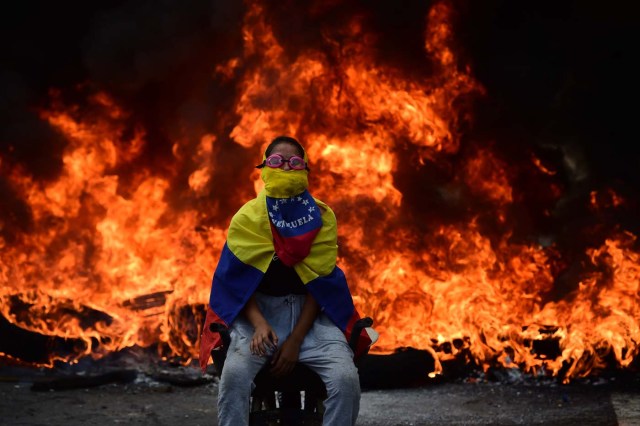 A Venezuelan opposition activist is backdropped by a burning barricade during a demonstration against President Nicolas Maduro in Caracas, on April 24, 2017. Protesters rallied on Monday vowing to block Venezuela's main roads to raise pressure on Maduro after three weeks of deadly unrest that have left 21 people dead. Riot police fired rubber bullets and tear gas to break up one of the first rallies in eastern Caracas early Monday while other groups were gathering elsewhere, the opposition said.  / AFP PHOTO / Ronaldo SCHEMIDT