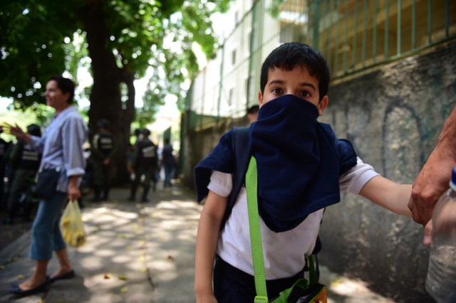 A child covers his nose and mouth to avoid breathing tear gas shot by police at opponents of Venezuelan President Nicolas Maduro marching in Caracas on April 26, 2017. Protesters in Venezuela plan a high-risk march against President Maduro Wednesday, sparking fears of fresh violence after demonstrations that have left 26 dead in the crisis-wracked country. / AFP PHOTO / RONALDO SCHEMIDT