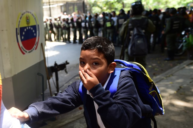 A schoolboy covers his nose and mouth to avoid breathing tear gas shot by police at opponents of Venezuelan President Nicolas Maduro marching in Caracas on April 26, 2017. Protesters in Venezuela plan a high-risk march against President Maduro Wednesday, sparking fears of fresh violence after demonstrations that have left 26 dead in the crisis-wracked country. / AFP PHOTO / RONALDO SCHEMIDT