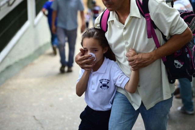 A schoolgirl covers her nose and mouth to avoid breathing tear gas shot by police at opponents of Venezuelan President Nicolas Maduro marching in Caracas on April 26, 2017. Protesters in Venezuela plan a high-risk march against President Maduro Wednesday, sparking fears of fresh violence after demonstrations that have left 26 dead in the crisis-wracked country. / AFP PHOTO / RONALDO SCHEMIDT