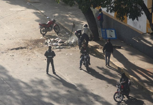 Los civiles armados y un oficial de la policía comienzan a retirar escombros de la vía pública después de reprimir a los manifestantes. R. R. 