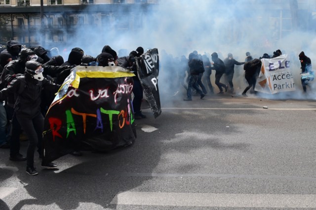 People hold banners as they march among fumes of smoke bombs during clashes taking place at a march for the annual May Day workers' rally in Paris on May 1, 2017. / AFP PHOTO / CHRISTOPHE ARCHAMBAULT